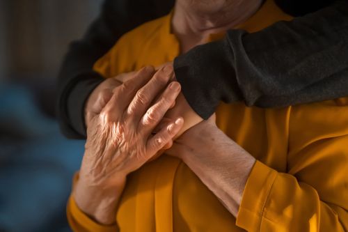 An adult son carefully hugs his beloved mother, closeup of their hands. Visual concept for a blog discussing nursing home care and how to ensure your parent's well-being and spot signs of abuse.
