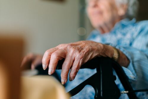 Close-Up Shot of a Caucasian Senior Woman Resting Her Hand on the Grip of her Mobility Walker while Sitting and Looking Out the Window