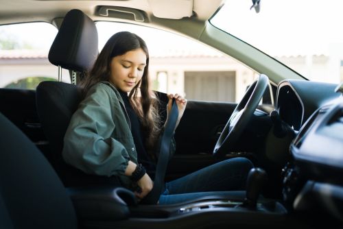 Teenage girl putting on her safety seatbelt and about to start the car. Teen driver getting ready to drive her new car